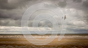 A second world war plane flying through storm clouds on the beach