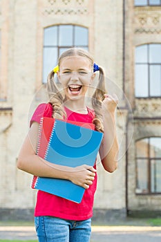 Secondary school student. Cute smiling small child hold books educational institution background. Adorable little girl