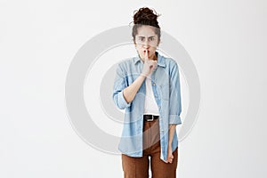 Secrecy, privacy and confidentiality. Frowning woman with hair in bun in denim shirt and serious strict look holding