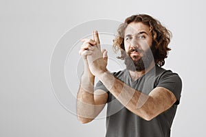 Secret agent on mission. Studio shot of playful serious-looking eastern man with beard making gun gesture and raising it