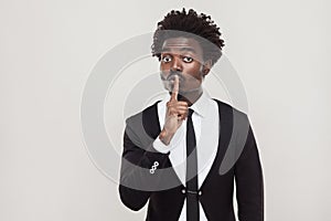 Secret or quiet concept. African businessman showing shh sign at photo