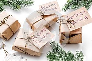 Secret Santa christmas game. Wrapped gift boxes with handwritten notes near spruce branch on white background close up