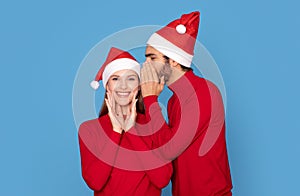 Secret Santa. Man Wearing Xmas Hat Whispering To His Excited Girlfriend's Ear