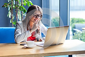 This is secret between us. Portrait of toothy smiley beautiful stylish young woman in glasses sitting, looking at monitor and