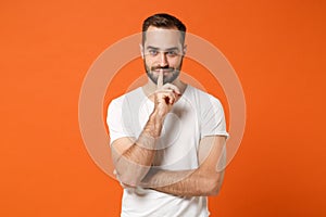 Secret young man in casual white t-shirt posing isolated on orange wall background studio portrait. People lifestyle