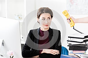 Secretary giving yellow stationary telephone to beautiful businesswoman