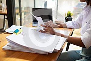 secretary searches through stacked documents on desk in office to find lease within stacked documents just before meeting. concept