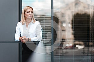 Beautiful blonde secretary stands sad near office windows