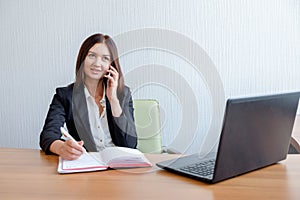 Secretary talking on mobile phone and writing notes while sitting at her desk.