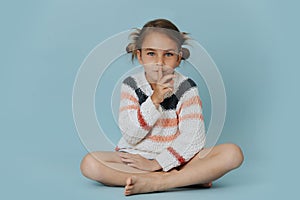 Secretive little girl sitting cross-legged with index finger over her lips