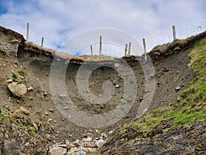 A section of a coastal walking path is lost due to erosion and landslip leaving fence posts hanging