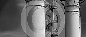 Section of a metal spiral staircase on an industrial building with two chimneys in black and white, copy space
