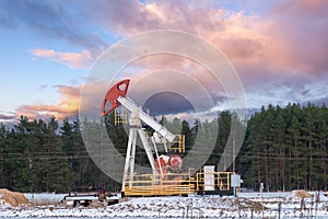 A section of an oil field, where oil pumps operate winter. Silhouette of a block pumping unit against a dramatic winter sky
