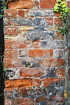 Section of an old red brick wall. There are cracks and damage and some ivy in the corner