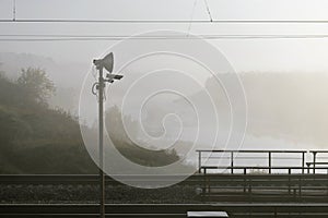 A section of the railway with a lamppost in the morning in a fog by the river.