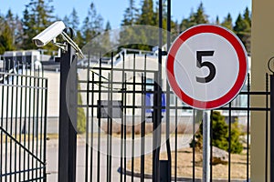 Secure entrance to the parking territory, surrounded by steel fence. Near the gate there is a video camera and a sign limiting the