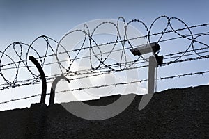 Security camera behind barbed wire fence around prison walls