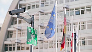 Security camera on a pole with a meeting point sign and EU flags behind