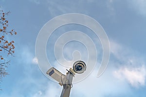 Security cameras against cloudy blue sky and tree