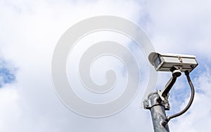 Security CCTV surveillance camera against a sky with big white c