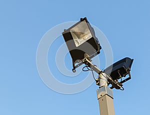 Security floodlights on a tall post against a winter blue sky at