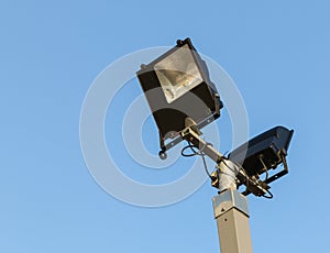 Security floodlights on a tall post against a winter blue sky at photo