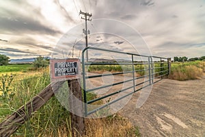 Security gate and fence with No Trespassing sign against mountain and cloudy sky