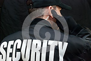 Security Guard Listens To Earpiece, Back of Jacket Showing