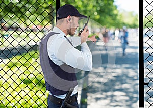 security guard of the park spiking with the walkie-talkie and point to something.