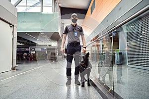 Security officer with detection dog standing in airport terminal