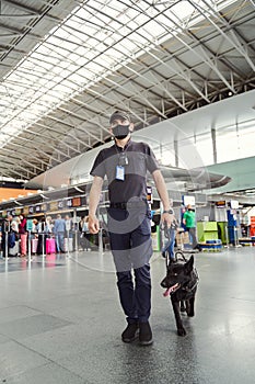 Security officer with detection dog walking down airport terminal