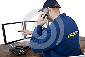 Security officer talking on phone while pointing at computer monitors