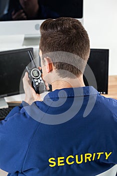 Security officer talking on walkie-talkie while looking at computer monitors