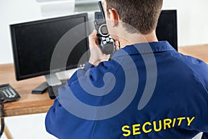 Security officer talking on walkie-talkie while looking at computer monitors