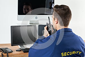 Security officer talking on walkie-talkie while looking at computer monitors