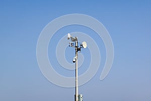 Security and satellite system with a surveillance camera, antenna and communications dishes on a pole against a sunny