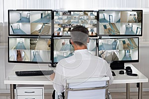 Security System Operator Looking At CCTV Footage At Desk photo