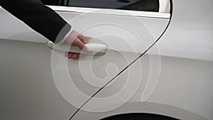 Sedan auto driver opening rear door of white luxury limousine vehicle.