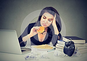 Sedentary lifestyle and junk food concept. Stressed woman sitting at desk eating hamburger photo