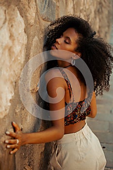 Seductive Afro-Columbian brunette with beautiful curly hair posing against a wall with closed eyes