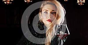 Seductive blonde in a green evening dress posing with a glass of red wine