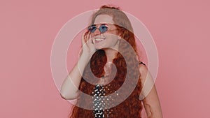 Seductive cheerful ginger stylish girl in dress wearing sunglasses, charming smile on pink wall