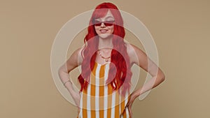 Seductive cheerful ginger stylish girl in tank top wearing sunglasses, charming smile on beige wall