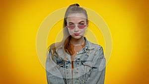 Seductive cheerful stylish girl in denim jacket wearing sunglasses, charming smile on yellow wall