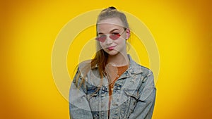 Seductive cheerful stylish girl in denim jacket wearing sunglasses, charming smile on yellow wall