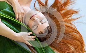 Seductive sensual portrait a young sexy woman with red hair loves nature and nestles on green decorative banana leaf, lying on the