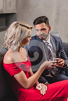 seductive stylish young couple holding glasses of red wine and looking