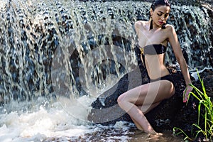 Seductive woman in black swimsuit on background waterfall
