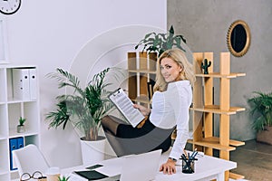 seductive woman sitting on table with documents and looking