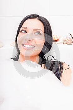 seductive young brunette blue eyes woman lying relaxing in the bath with foam happy smiling & looking aside closeup portrait